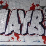 Graffiti in blue and red outline against a white wall that reads "Maybe"