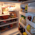 An open refrigerator with various food stuffs in it, such as milk, soda, and condiments